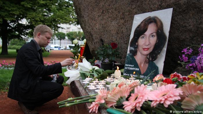 Фото с портретом Натальи Эстемировой, перед которым лежат цветы и стоят свечи в память о ней