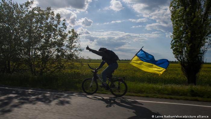 Велосипедист едет по дороге в регионе между Николаевом и Херсоном с флагом Украины, 15 мая 2022 года
