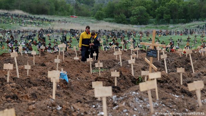 Двое жителей Мариуполя на кладбище со свежими могилами в месте Старый Крым на окраине города Мариуполь, 22 мая 2022 года.